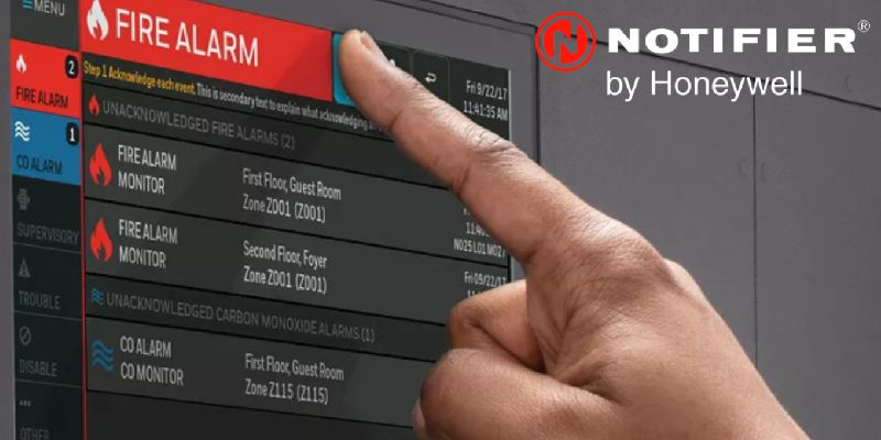 A hand operating a fire panel with a NOTIFIER logo behind