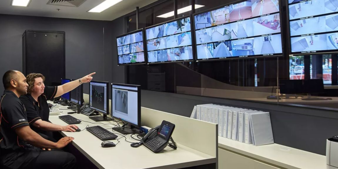 two people sitting in front of a large bank of security screens