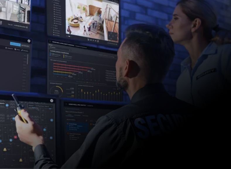 An image showing two people looking at a bank of security screens