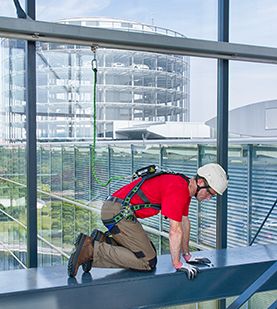 Worker in a Miller Revolution safety harness and a Miller Edge-tested fall arrest lanyard uses a MultiRail horizontal anchorage system to access a glazed curtain wall in complete safety