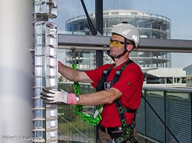 Worker in a Miller Revolution safety harness and a Miller Edge-tested fall arrest lanyard uses a MultiRail horizontal anchorage system to access a glazed curtain wall in complete safety