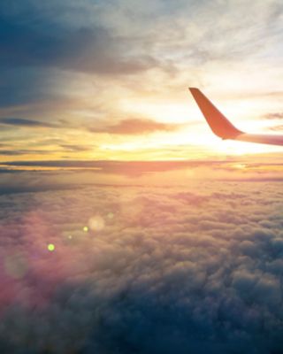 Wing of an airplane flying above the sunriseclouds and flare effect