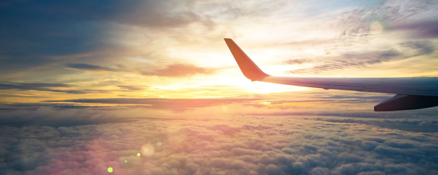 Wing of an airplane flying above the sunriseclouds and flare effect