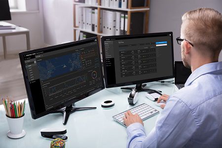 A man working in a computer with 2 monitors