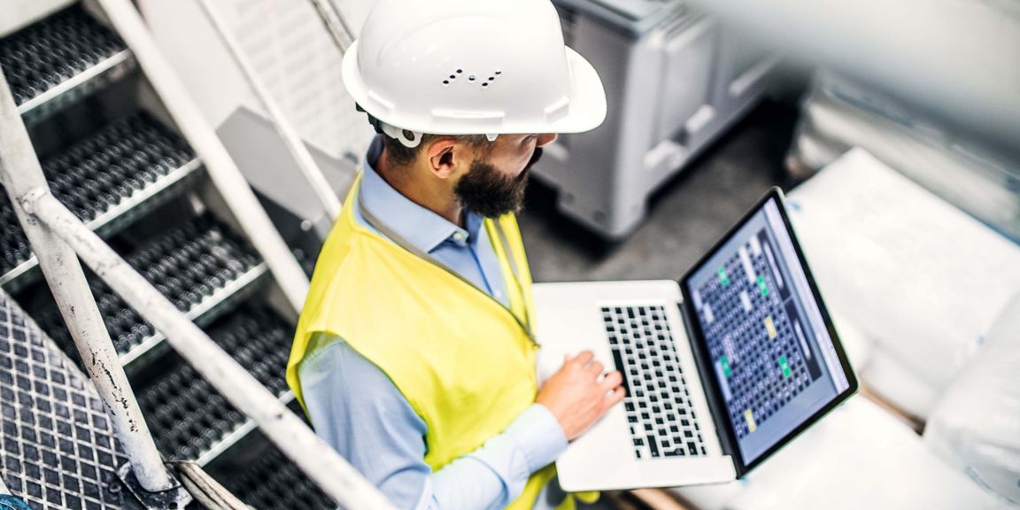 A portrait of a mature industrial man engineer with laptop in a factory, working. High-angle view.