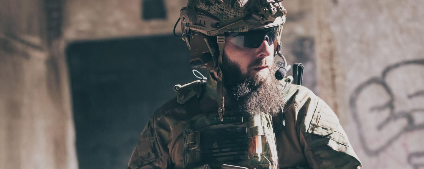 Soldier in tactical gear and helmet with communication headset standing in a low-light environment, representing modern defense operations.