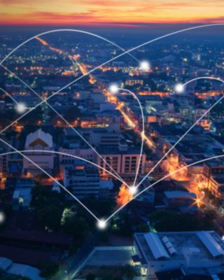 Aerial view of a brightly lit city at dusk with glowing connection lines symbolizing global communication and network connectivity.