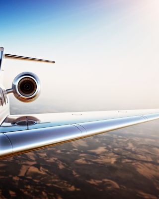 Photo of White Luxury Generic Design Private Jet Flying in Blue Sky at sunset.Uninhabited Desert Mountains Background.Business Travel Picture.Horizontal,Film Effect. 3D rendering