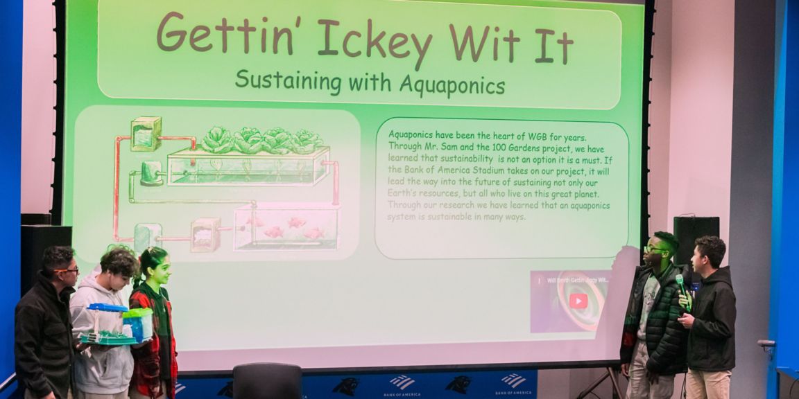 Students present their project - "Sustaining with Aquaponics" - pictured on a stage with a slideshow about their plan to implement aquaponic produce at the stadium.