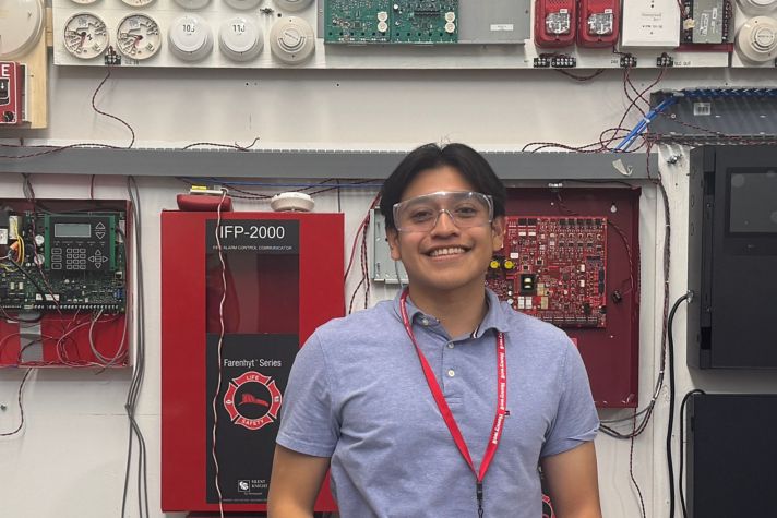 Certification engineer Edwin Rosales smiles in front of a wall with Honeywell fire safety technologies.