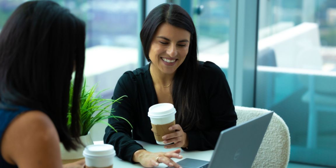 Two people are collaborating in a lounge area at the Honeywell headquarters building. One has a cup of coffee in their hand and they are collaborating on a laptop.