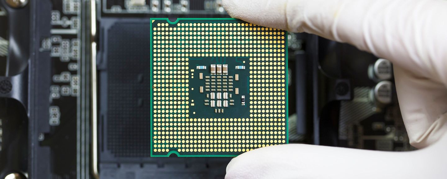 Close-up photo of a semiconductor -- a gloved hand holds the microchip.