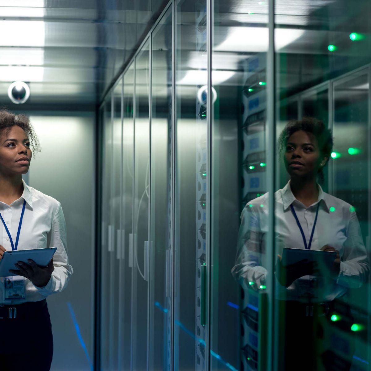 African American woman using tablet while walking in corridor of data center and checking hardware on server racks