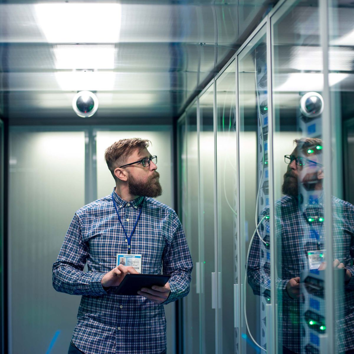 Wide shot of casual man with tablet walking among server racks in data center room looking at hardware