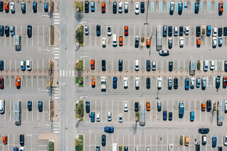 An overhead drone perspective captures the structured layout and organized rows of a busy commercial parking lot filled with various vehicles.
