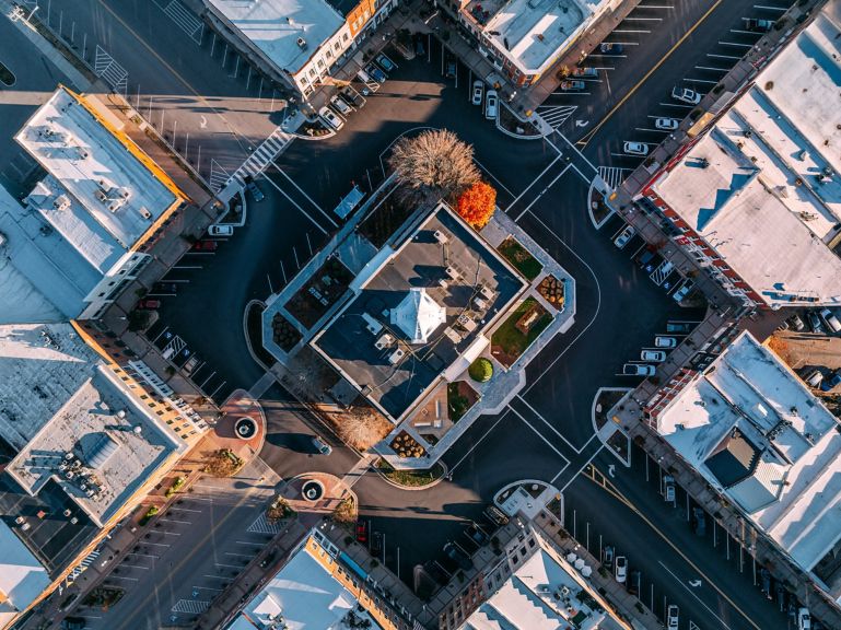 An overhead drone perspective captures the geometric layout of a historic town center at sunset, highlighting the central building and surrounding street grid.