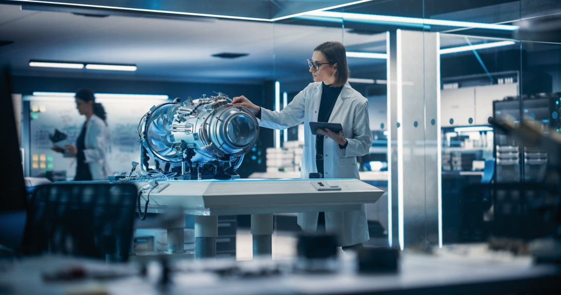 A scientist in a lab coat inspects a prototype jet turbine component using a digital tablet in a high-tech corporate research facility.