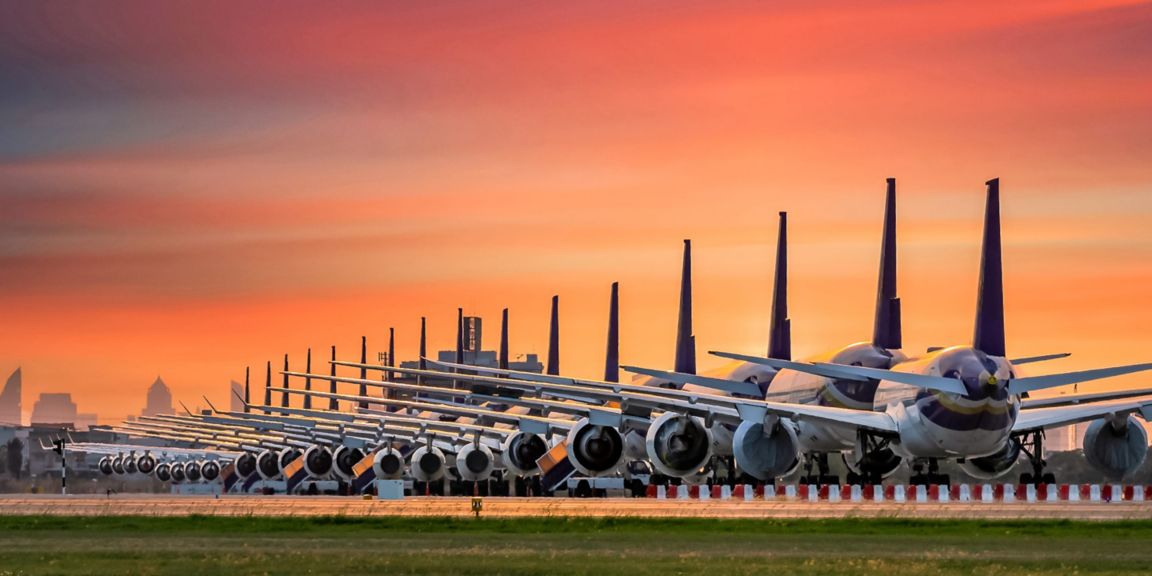 Large fleet of airplanes parked in line on an airport runway during a vibrant sunset, showcasing aviation scale and symmetry.
