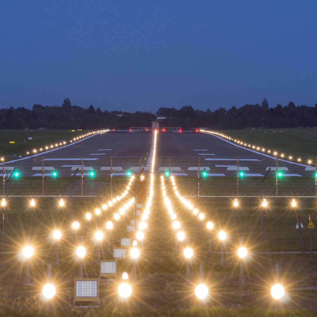 A symmetric low-angle view of airport approach lighting systems guiding aircraft onto the runway during twilight.