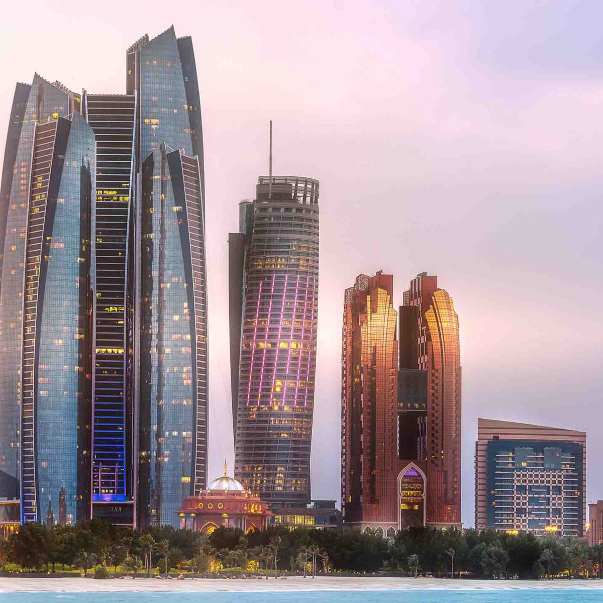 A panoramic view of Abu Dhabi’s skyline at dusk, showcasing modern skyscrapers alongside the ornate Emirates Palace, lit up against a twilight sky.