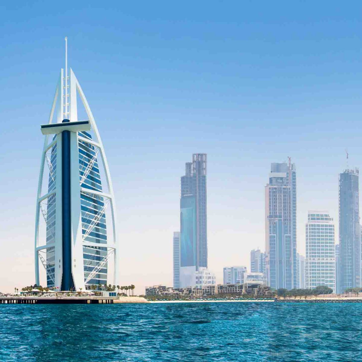 Stunning view of Dubai's skyline featuring the iconic Burj Al Arab and modern skyscrapers against a clear blue sky and the Arabian Gulf.