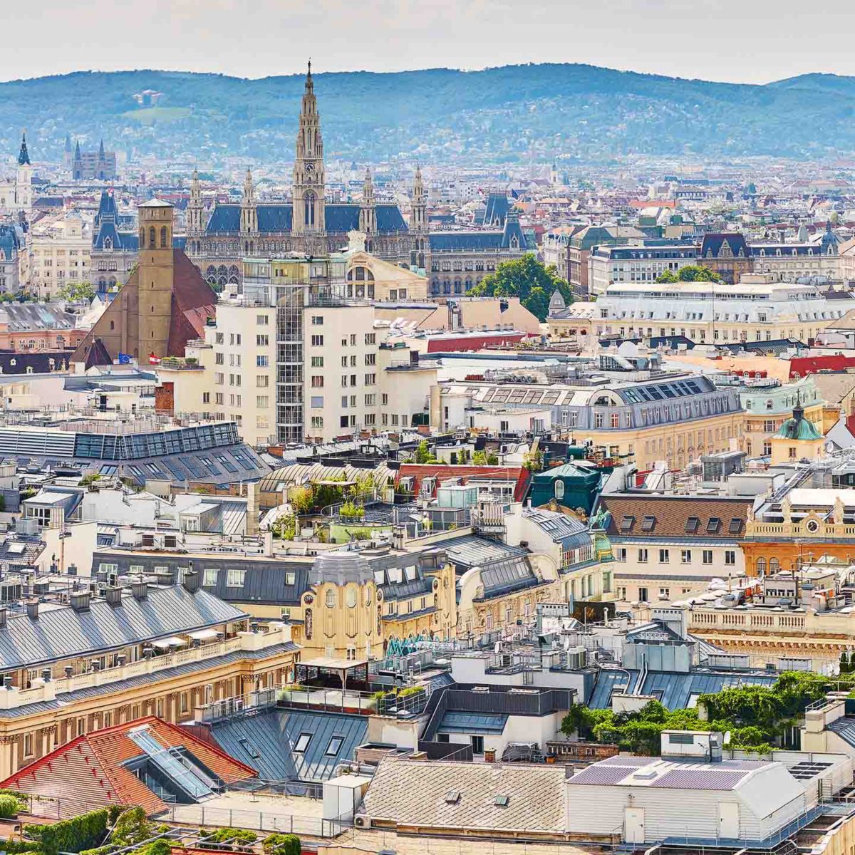 A stunning aerial view of Vienna, showcasing historic architecture, rooftops, and distant hills under a cloudy sky.