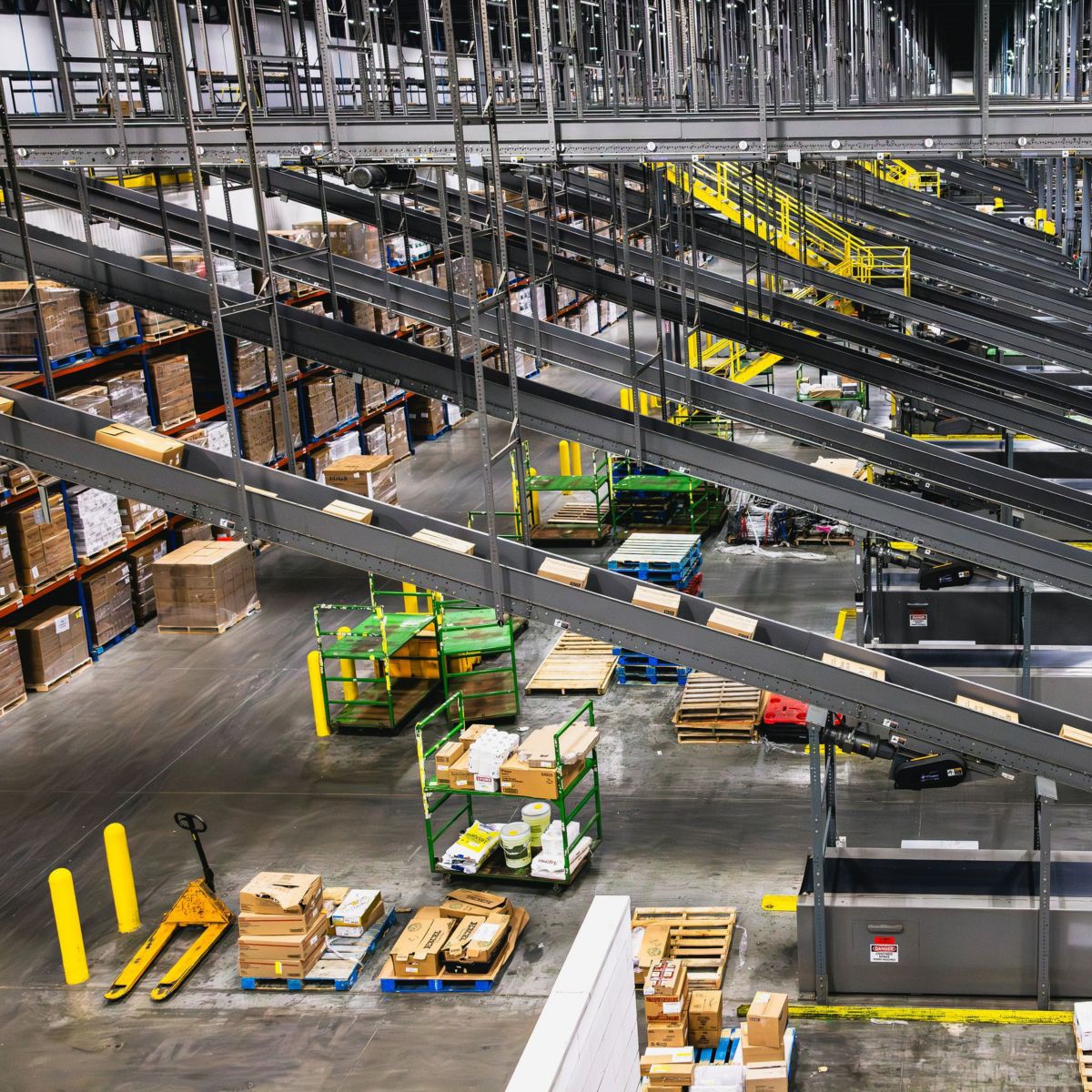 A high-angle view of a modern industrial distribution center featuring complex overhead conveyor belts and organized pallet logistics.