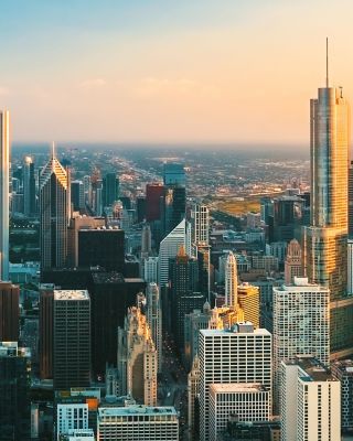 Tall buildings reflect sunset near lake and distant horizon.