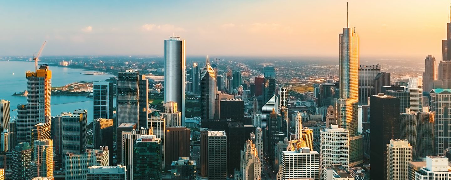 Tall buildings reflect sunset near lake and distant horizon.