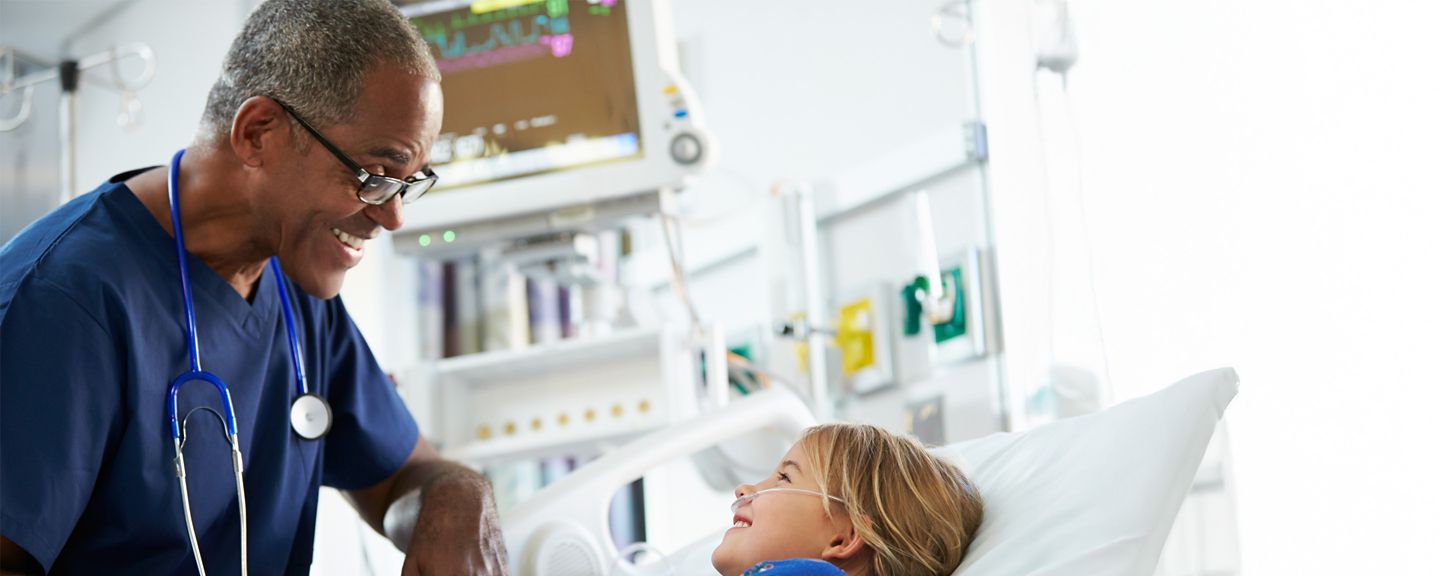 Doctor speaks to patient resting in hospital bed, equipment nearby.