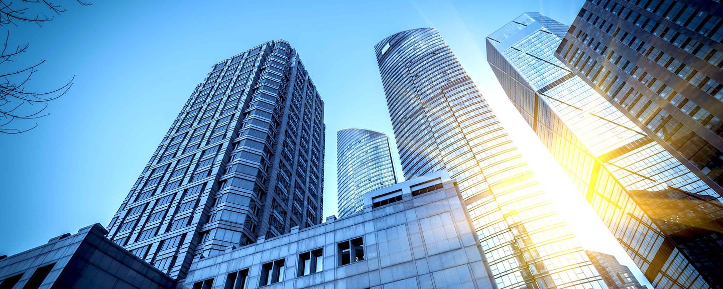 A stunning view of modern skyscrapers in an urban cityscape, captured from a low angle with sunlight reflecting off the glass surfaces. The image showcases the architectural beauty and grandeur of tall buildings against a clear blue sky.