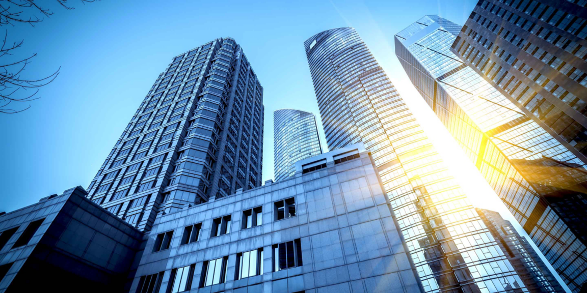 A stunning view of modern skyscrapers in an urban cityscape, captured from a low angle with sunlight reflecting off the glass surfaces. The image showcases the architectural beauty and grandeur of tall buildings against a clear blue sky.