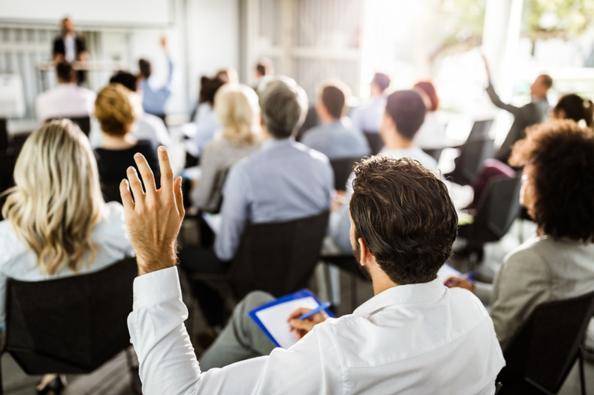 Rear view of a businessman raising his hand to ask the question on a seminar with large group of his colleagues.