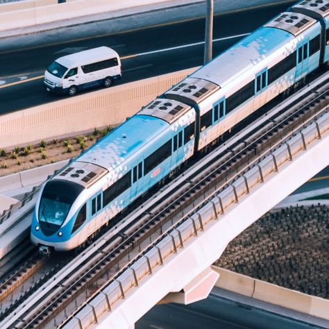 A sleek blue and white elevated train crosses a concrete bridge above a busy road with a white van below. Ideal for showcasing urban transportation, infrastructure, or smart city mobility solutions.