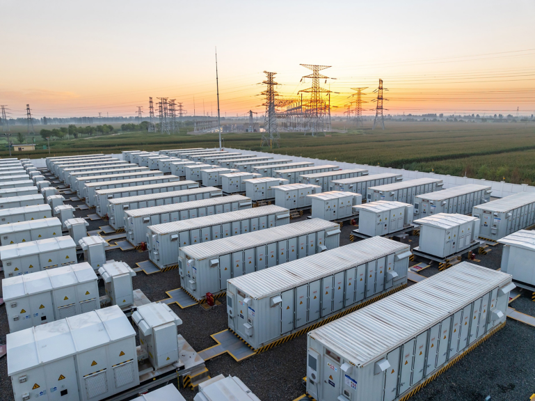 Aerial view of a large-scale industrial battery energy storage system at sunset near high-voltage transmission towers.