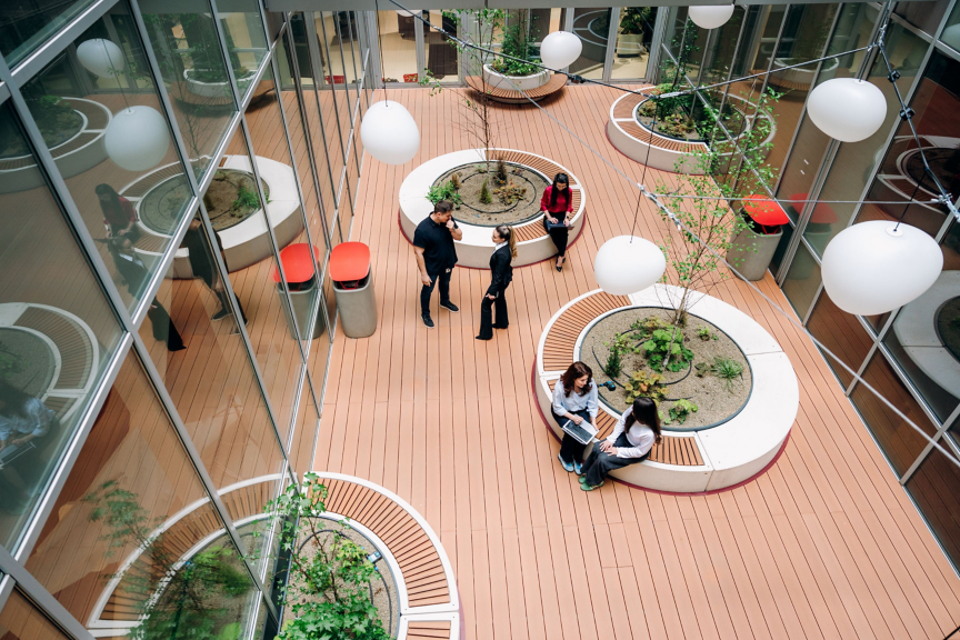 A spacious indoor courtyard featuring plants, seating areas, and people engaged in conversation and work.