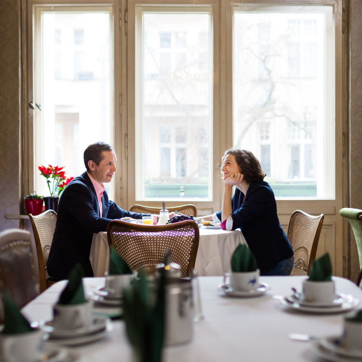 A professional man and woman have an engaging business meeting over breakfast in a brightly lit, elegant restaurant setting.