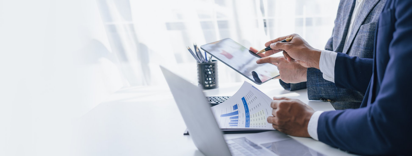 Business professionals use a tablet while reviewing printed charts and financial data.
