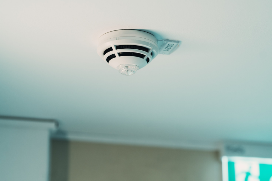 A close-up view of a white fire alarm smoke detector securely mounted on an indoor office ceiling.
