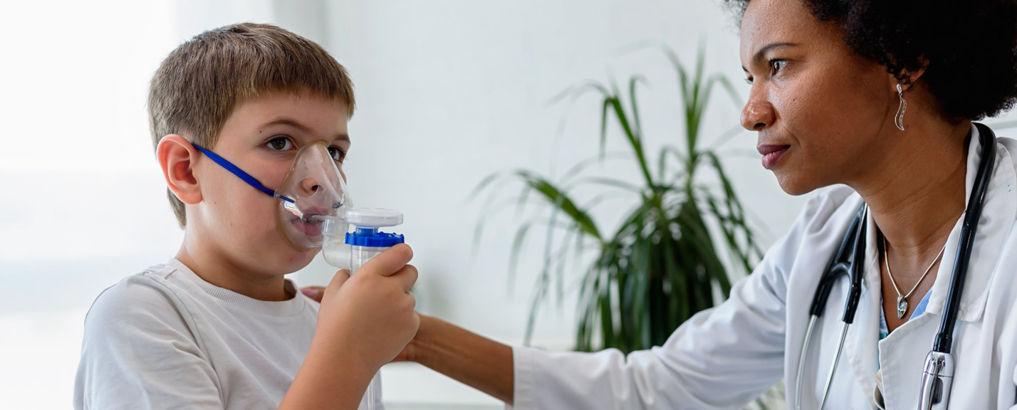 A child breathes through a respiratory device while a clinician provides support.