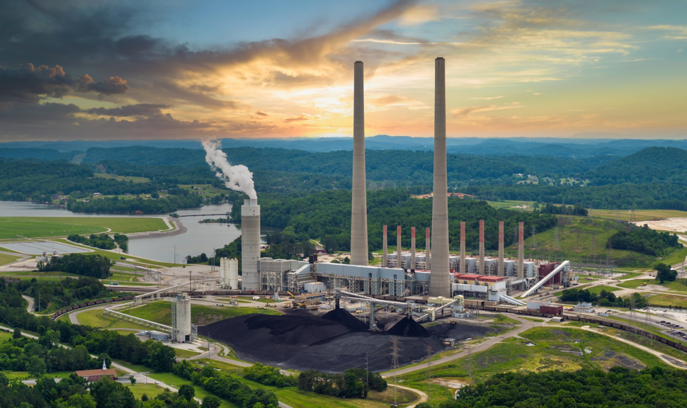 Aerial view of a large coal-fired power station operating near a river under a dramatic sunset sky.
