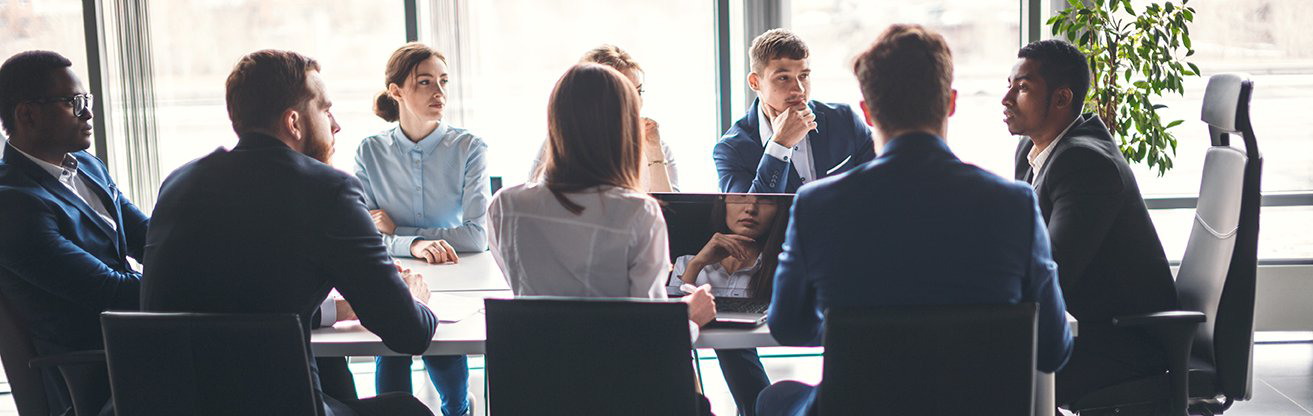 A diverse group of colleagues discuss work around a conference table in a bright office.