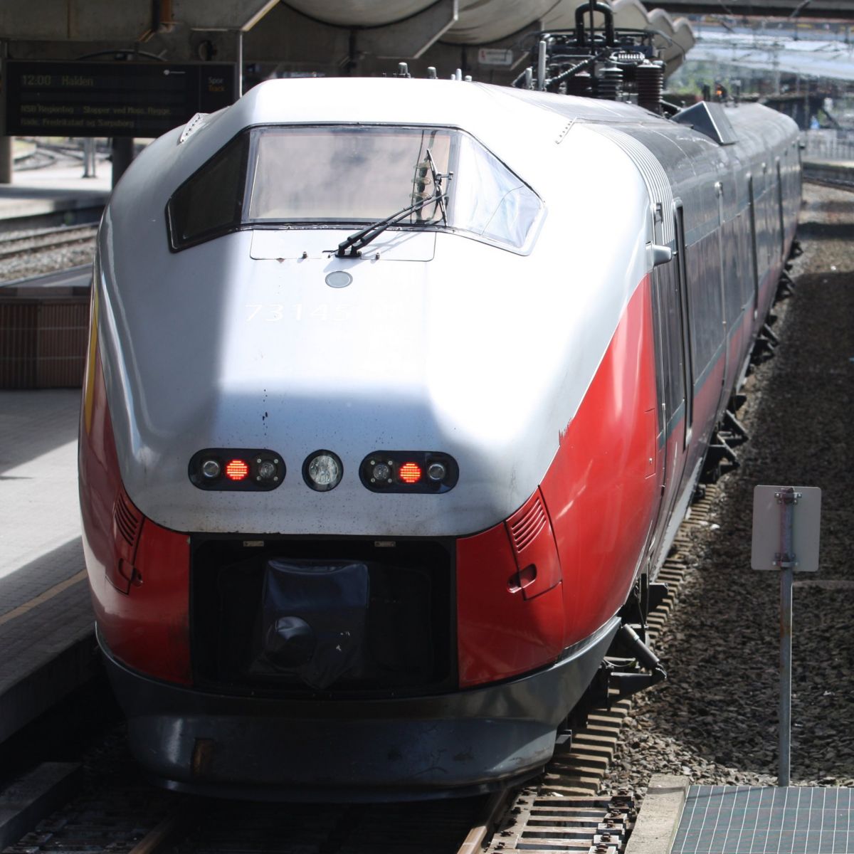 Two modern red and silver electric commuter trains sit side-by-side at a railway station platform.