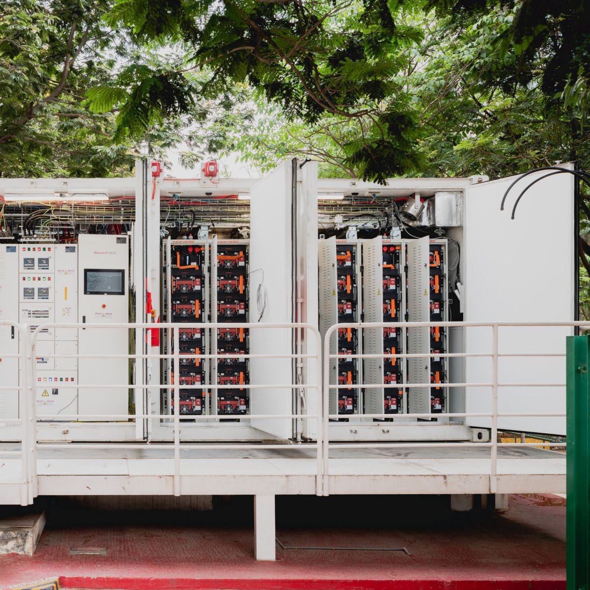 A high-angle exterior view of a containerized battery energy storage system featuring exposed control panels and internal modular racks.