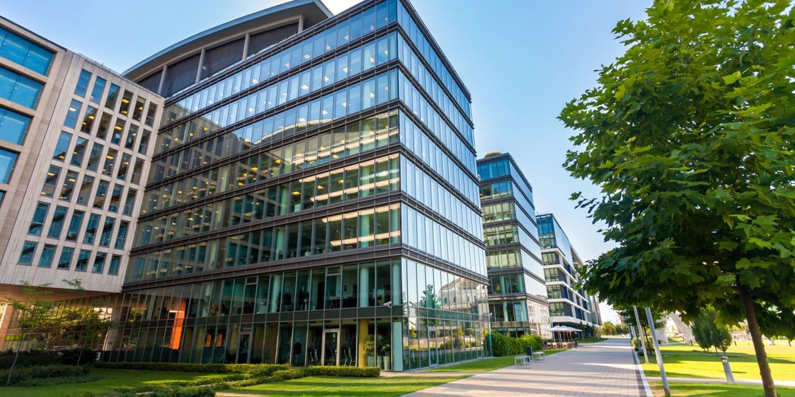 This image showcases an impressive modern office building characterized by its sleek glass facade, reflecting the bright blue sky and surrounding greenery. The structure features multiple floors and large windows, allowing natural light to fill the interior spaces. The well-manicured landscaping and pathway invite visitors to explore the stylish exterior, which seamlessly blends with the urban environment. The image captures a vibrant atmosphere indicative of a contemporary corporate setting, ideal for hosting business activities and fostering collaboration among professionals. The lush trees and open spaces further enhance the aesthetic appeal, creating a harmonious balance between nature and urban architecture. This scene exemplifies the evolution of modern workplaces, where design prioritizes both functionality and visual elegance, making it an ideal representation of a forward-thinking office environment.