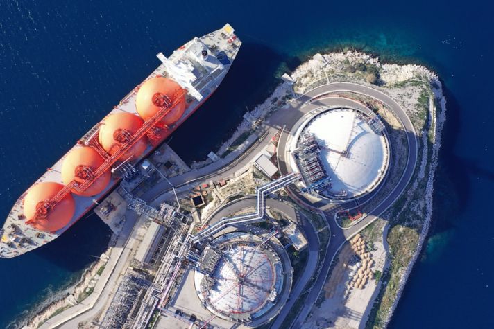 Aerial drone top down photo of LNG (Liquified Natural Gas) tanker anchored in small gas terminal island with tanks for storage to store and regasify LNG