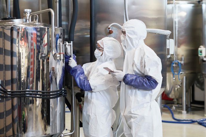 Wide angle view at two workers wearing protective suits while inspecting production at modern chemical plant
