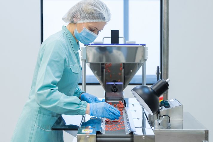 A technician in protective clothing manages equipment in a life science lab, focusing on precise handling of materials in a sterile environment.