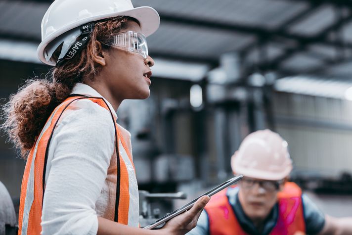 Two construction workers in safety gear, focused on their tasks in a factory environment, highlighting teamwork and safety practices.