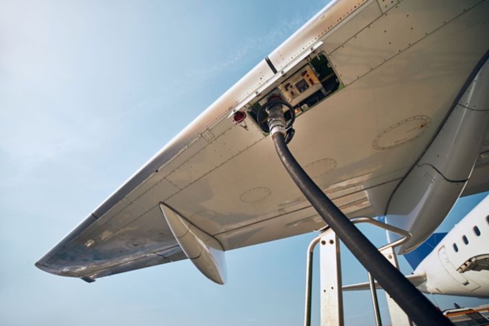 An airplane wing with a fuel hose attached for refueling, showcasing the aircraft against a bright blue sky.